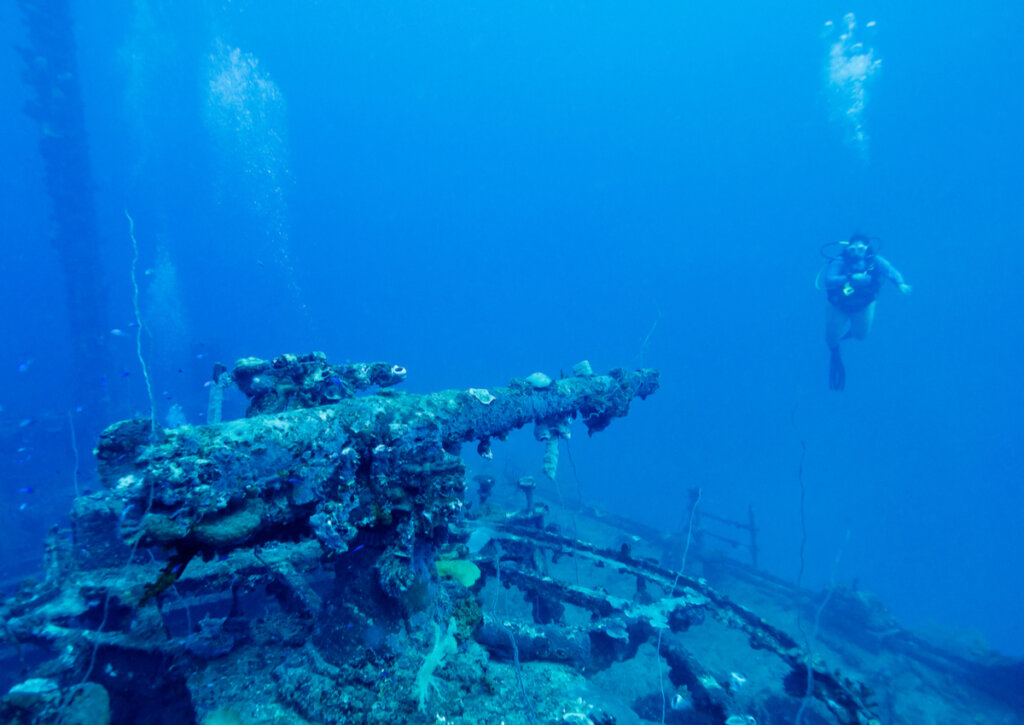 Turista buceando en el atolón Truk, cerca de una ametralladora hundida.