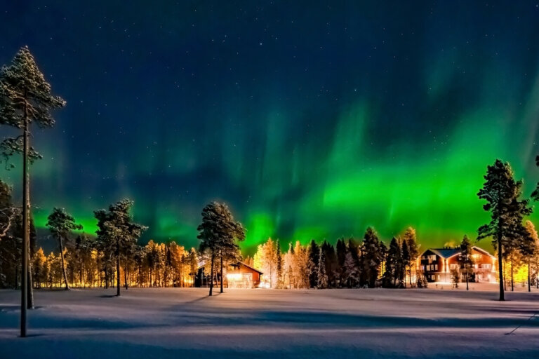 Casas en medio del bosque con nieve y aurora boreal